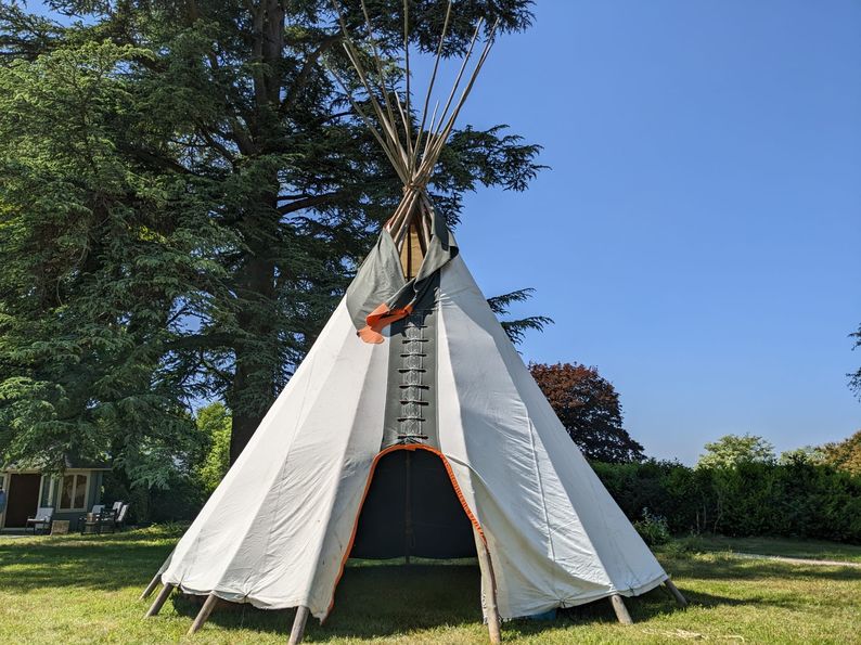 A white tipi stands under the shade of a tree