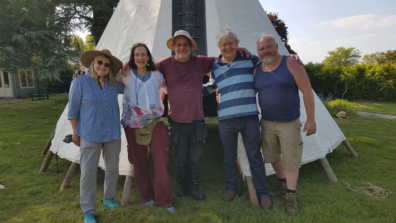 Five people linking arms in front of  a tipi