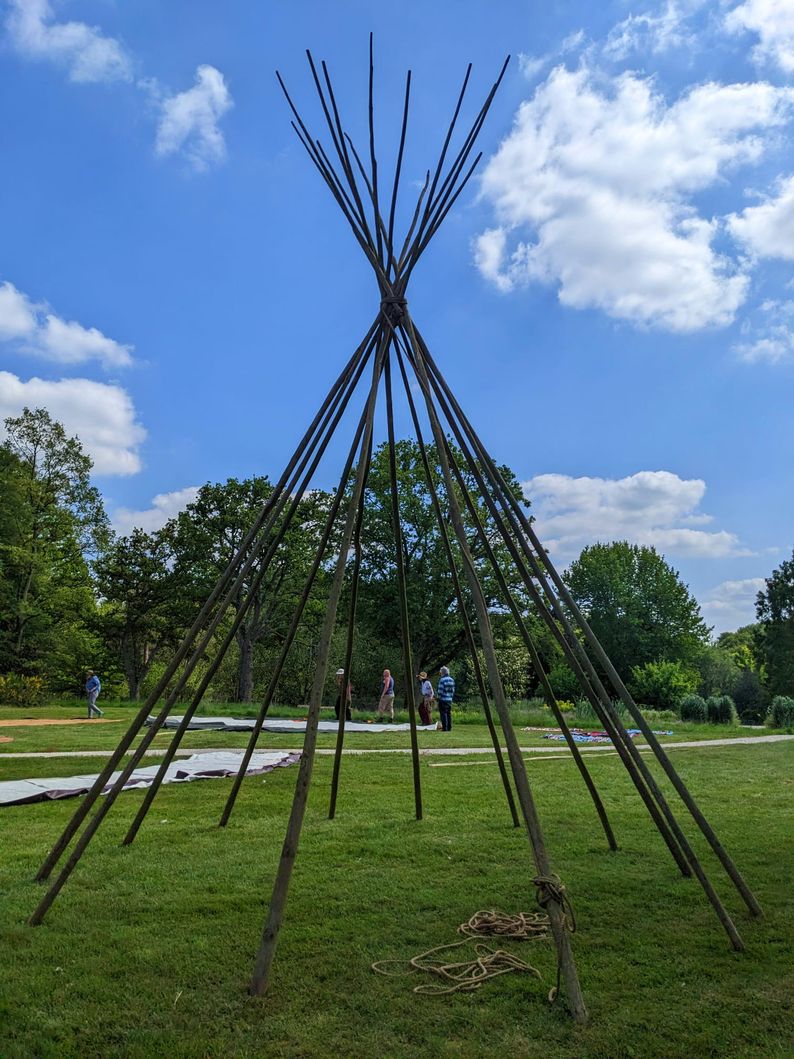The wooden skeleton of a tipi in the foreground under a blue sky